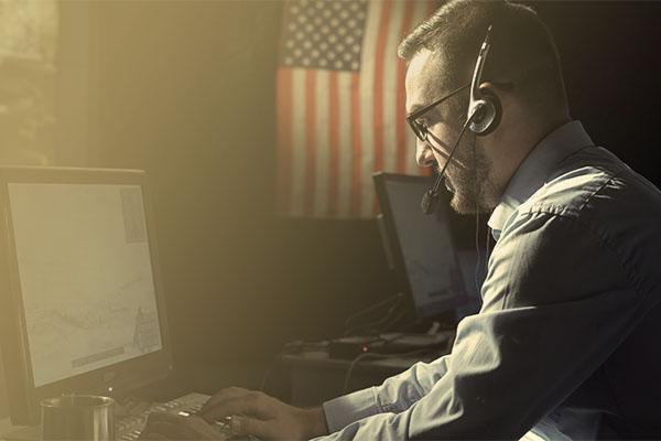 man wearing headset at computer with American flag in background