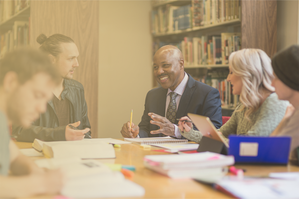 Higher education administration professionals in discussion with students in a library setting