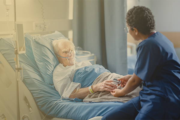 Image of nurse helping an older male patient who is lying in a hospital bed