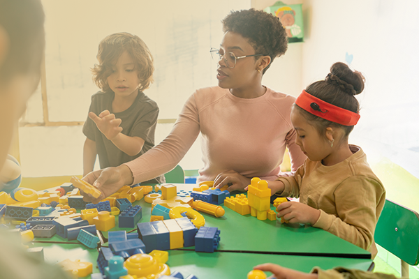 Image of a teacher working with two children playing a block building game in a classroom.